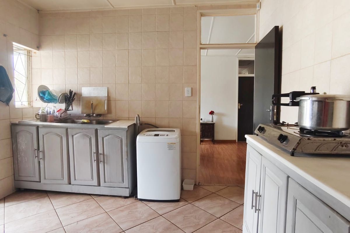 A functional kitchen featuring tiled walls and flooring, built-in cabinetry, a stainless steel sink, and a gas hob, with an adjacent room visible.