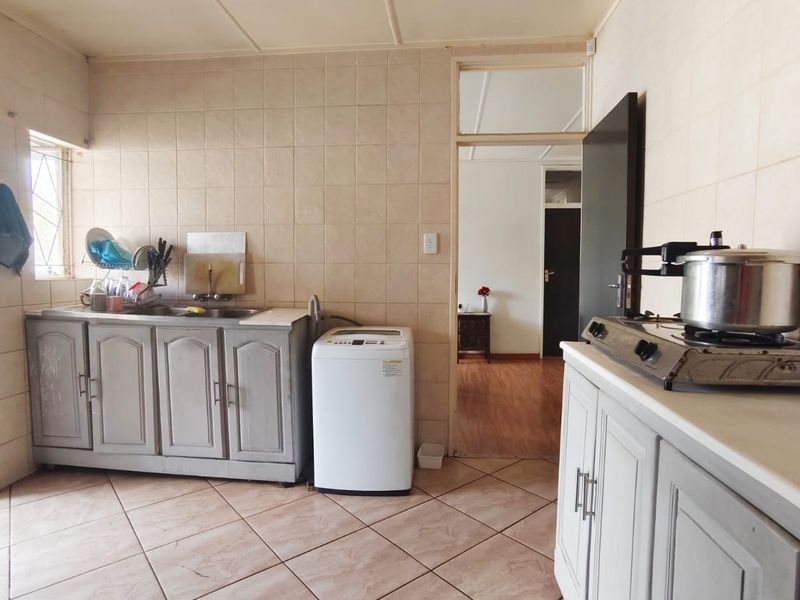 A functional kitchen featuring tiled walls and flooring, built-in cabinetry, a stainless steel sink, and a gas hob, with an adjacent room visible.