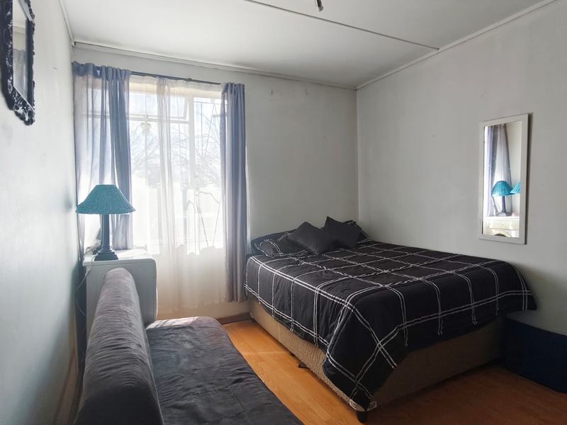 A bedroom featuring laminate flooring, track lighting, and a window. The room shows signs of wear on the walls and ceiling.