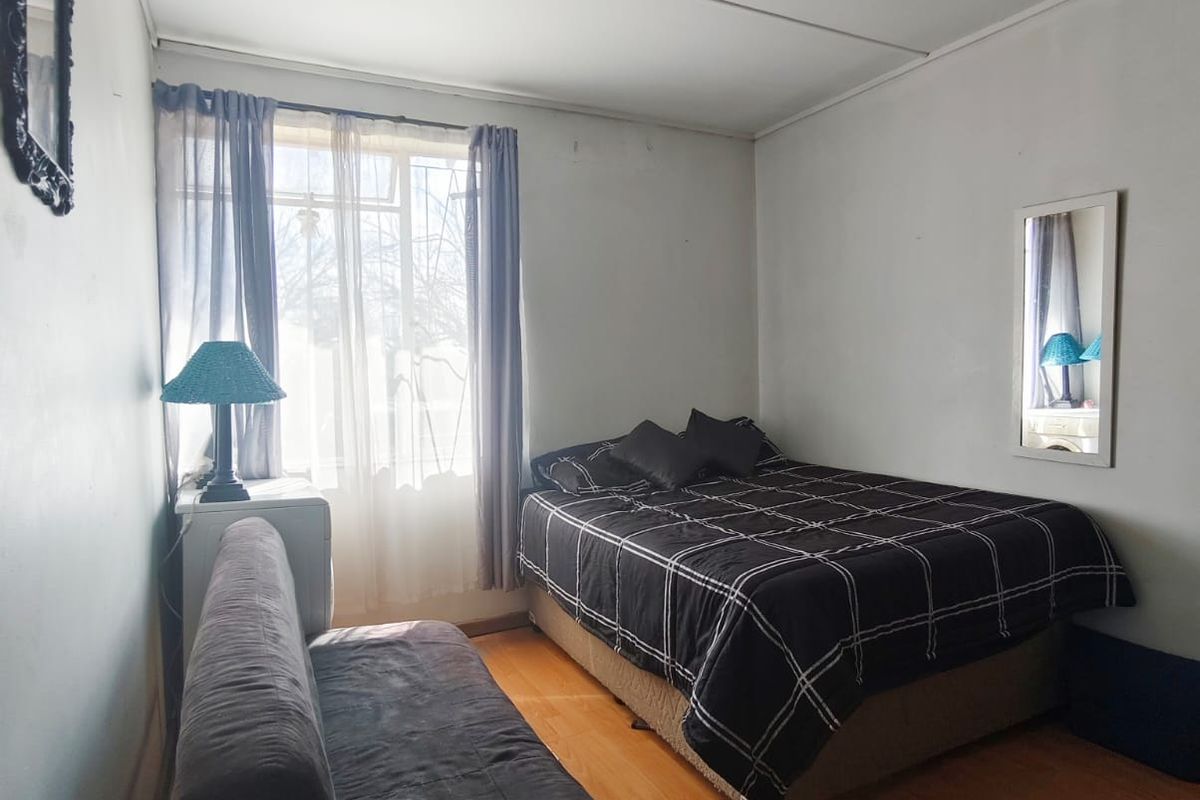 A bedroom featuring laminate flooring, track lighting, and a window. The room shows signs of wear on the walls and ceiling.