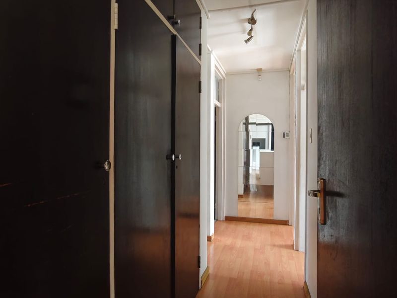A functional hallway featuring extensive built-in storage cupboards and laminate flooring, leading towards an arched doorway.