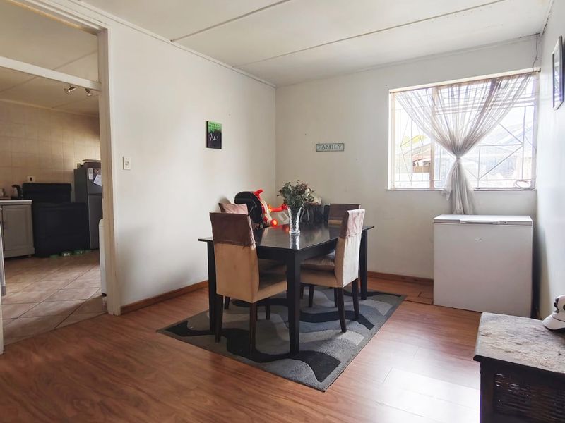 Dining area featuring laminate flooring and a window with security bars, providing a functional space with direct access to the adjacent kitchen.