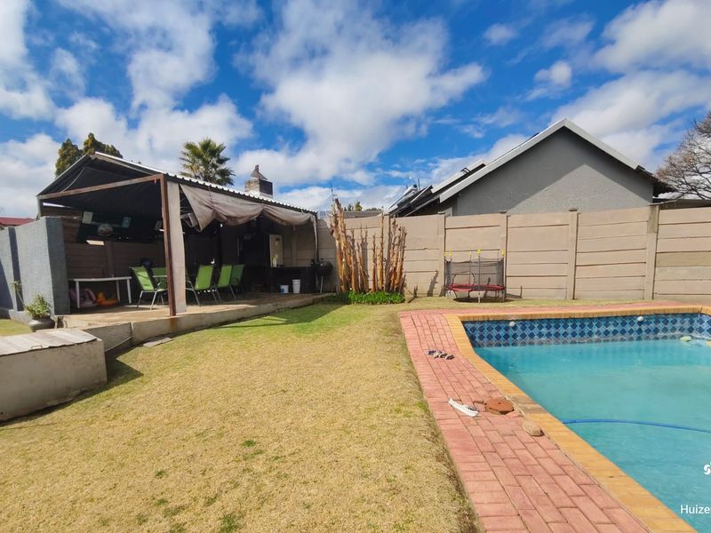 Outdoor entertainment area featuring a swimming pool with brick coping, a covered patio with a built-in braai, and a private garden.