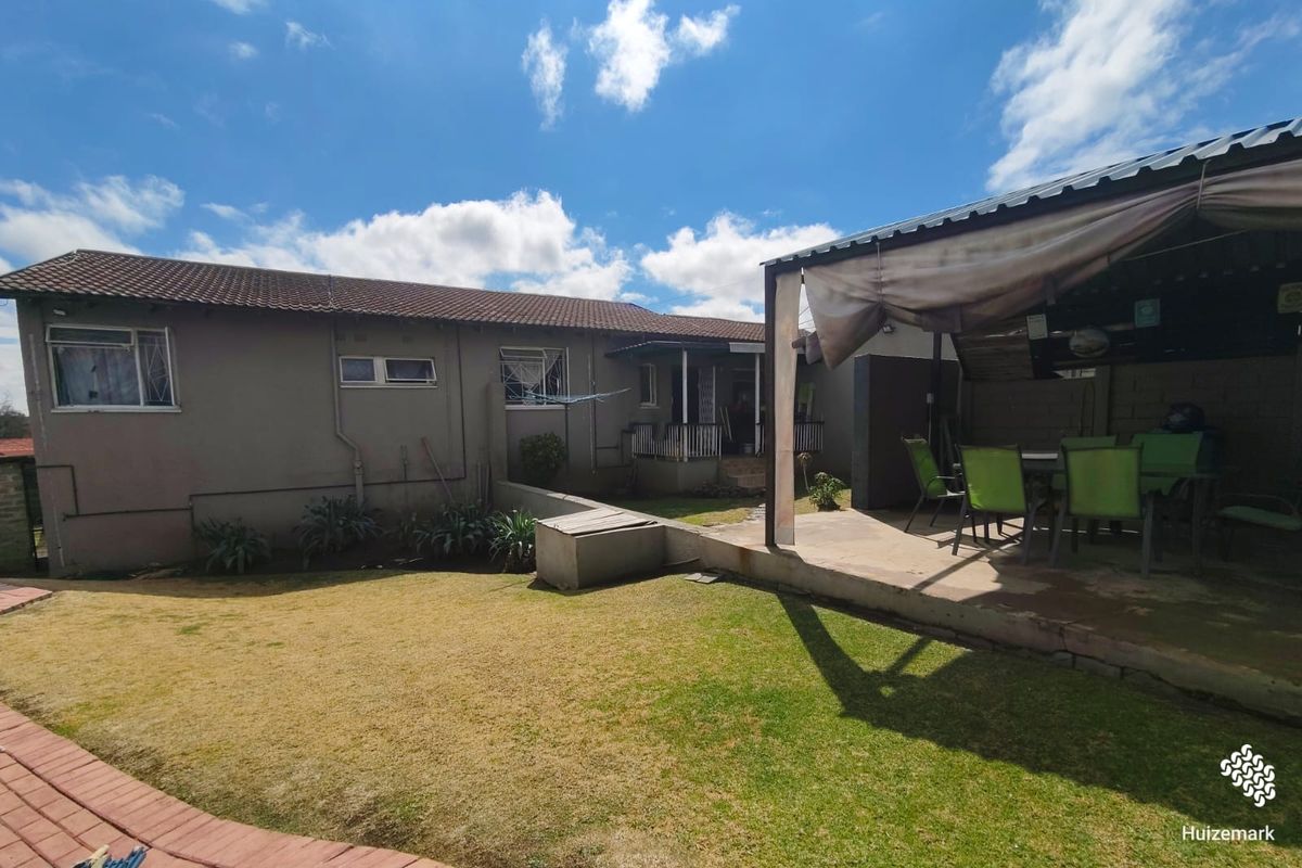 Rear view of the property featuring a covered patio area, lawn, and paved pathways, providing a functional outdoor space for relaxation.
