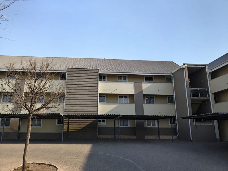 Front elevation of a multi-story residential apartment complex featuring covered parking bays and a paved driveway area.