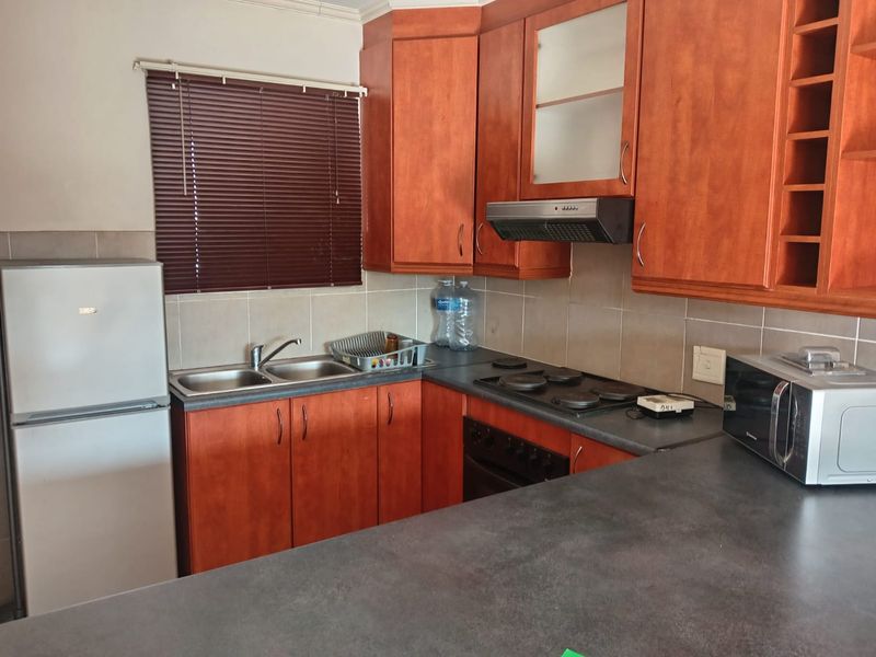 Functional kitchen featuring warm-toned cabinetry, dark laminate countertops, a double sink, and built-in cooking appliances with a tiled splashback.