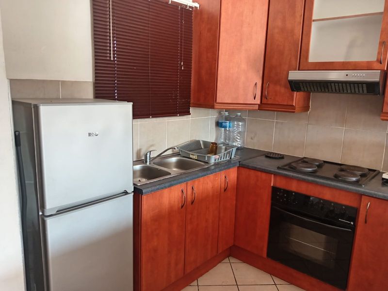 A functional kitchen featuring wooden cabinetry, laminate countertops, a double basin sink, and built-in cooking appliances including an oven and electric hob.