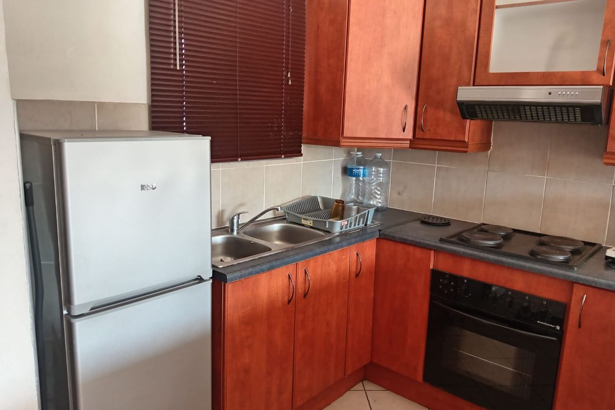 A functional kitchen featuring wooden cabinetry, laminate countertops, a double basin sink, and built-in cooking appliances including an oven and electric hob.