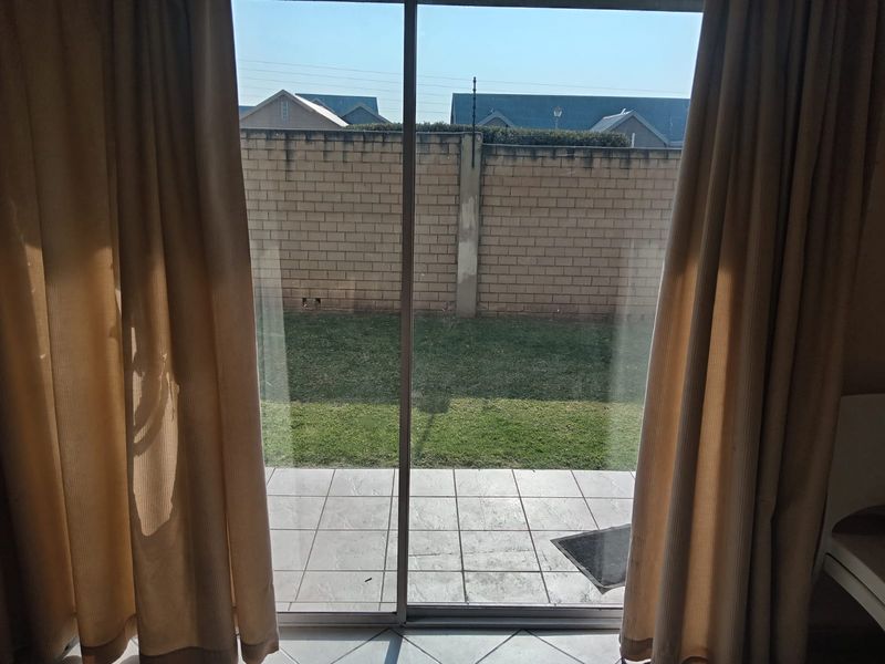 View from an interior room through a sliding glass door onto a tiled patio and private garden with a brick boundary wall.