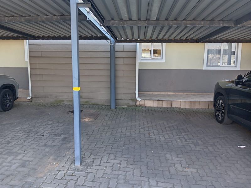 A covered carport area featuring a metal structure, paved driveway, and direct access to the building entrance.