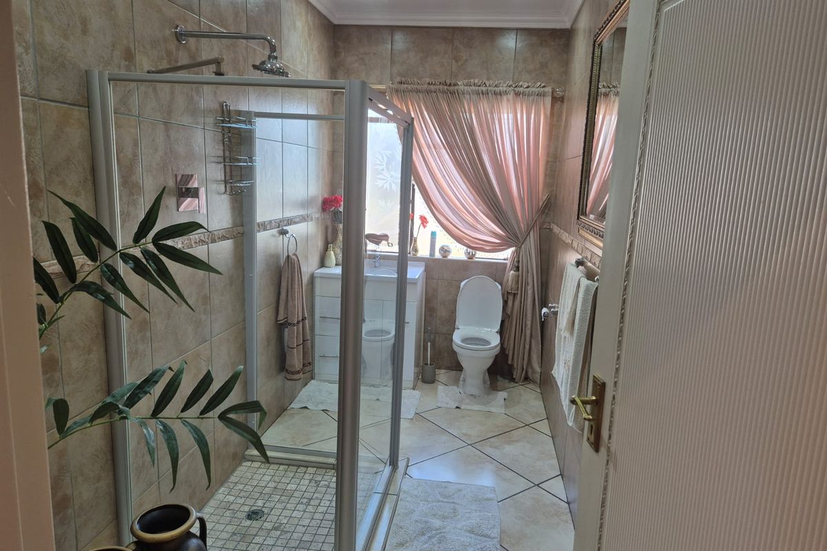 A functional bathroom featuring a glass-enclosed shower, vanity cabinet, toilet, and neutral-toned wall and floor tiling.