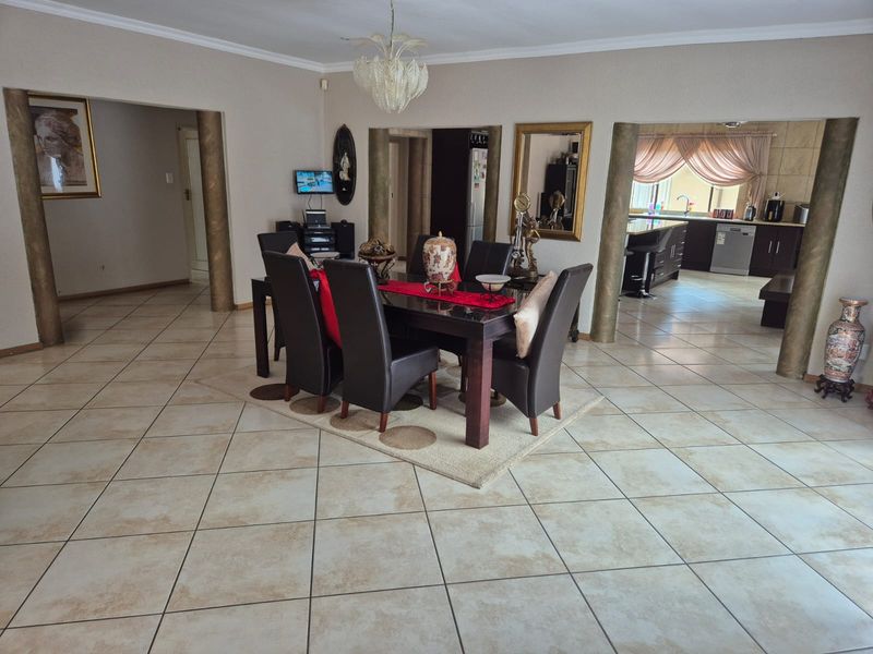 Spacious open-plan dining area featuring tiled flooring and decorative columns, with a clear view into the adjacent kitchen space.