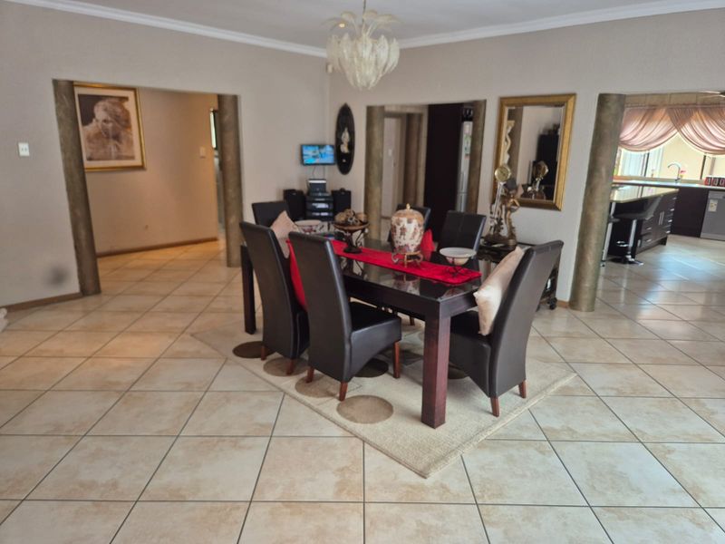 Spacious open-plan dining area featuring ceramic floor tiles, decorative columns, and coved ceiling cornices, with a view into the adjacent kitchen.