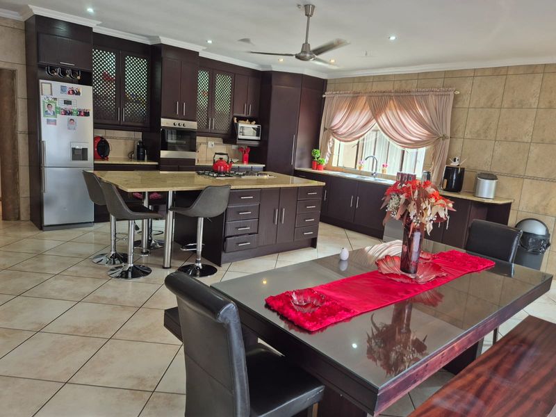 Spacious open-plan kitchen and dining area featuring dark wood cabinetry, granite countertops, a central island, and tiled flooring throughout.
