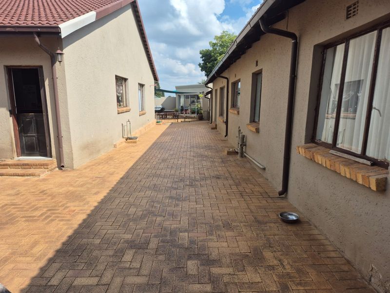A paved side walkway between two sections of the house, featuring exterior brick sills and functional drainage downpipes.