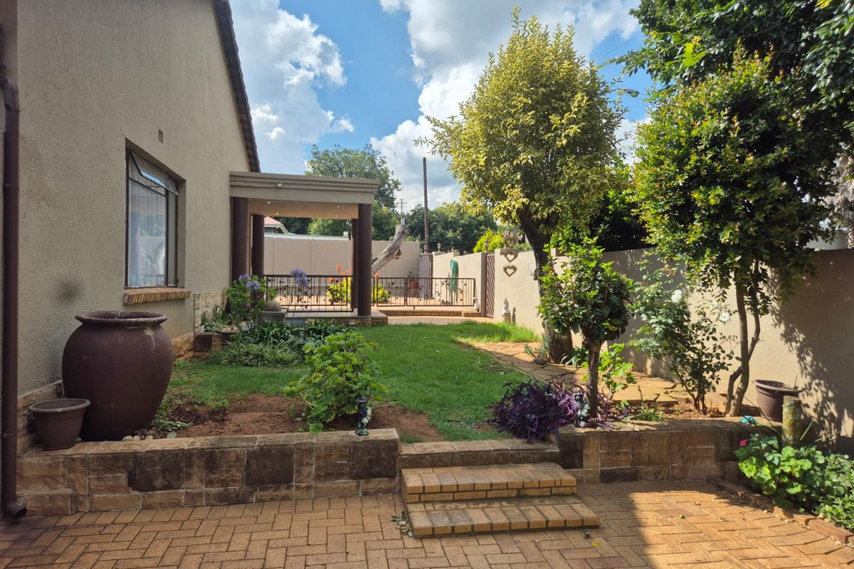 A well-maintained rear garden featuring a paved patio area, brick retaining walls, and a covered outdoor entertainment space.