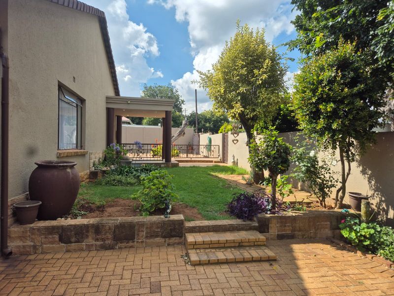 A well-maintained rear garden featuring a paved patio area, brick retaining walls, and a covered outdoor entertainment space.