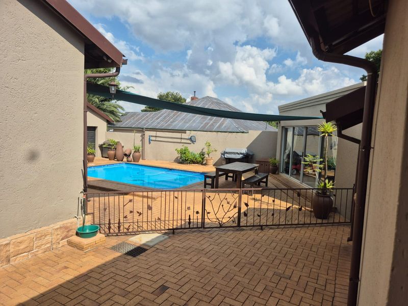 A private outdoor pool area featuring a paved patio, metal safety fencing, and a shade sail, providing a functional space for outdoor relaxation.