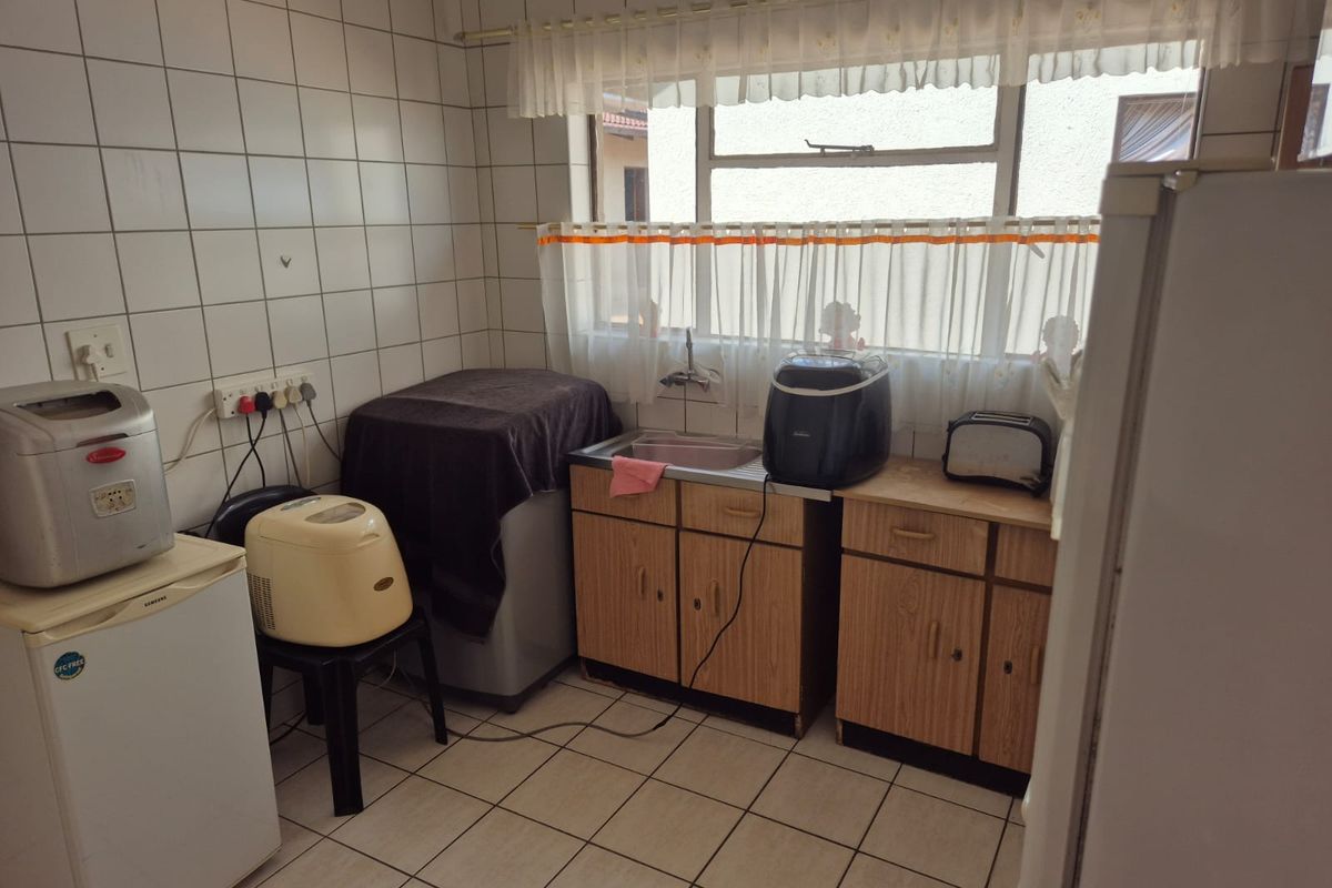 A functional kitchen space featuring tiled walls and flooring, a single basin sink, and dated wooden cabinetry under a window.