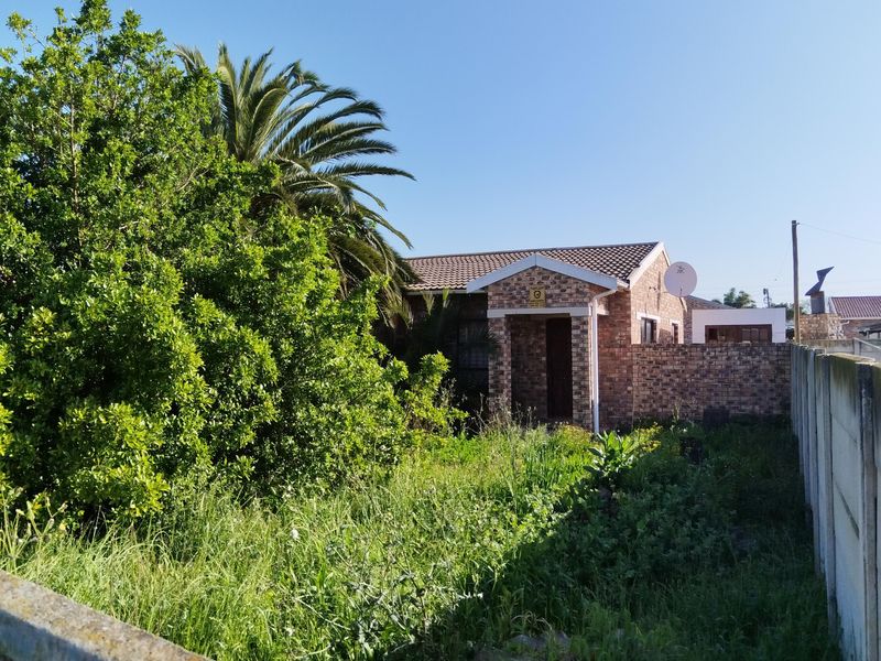 Front view of a face brick house featuring a tiled roof and a large, overgrown garden area enclosed by a precast concrete boundary wall.