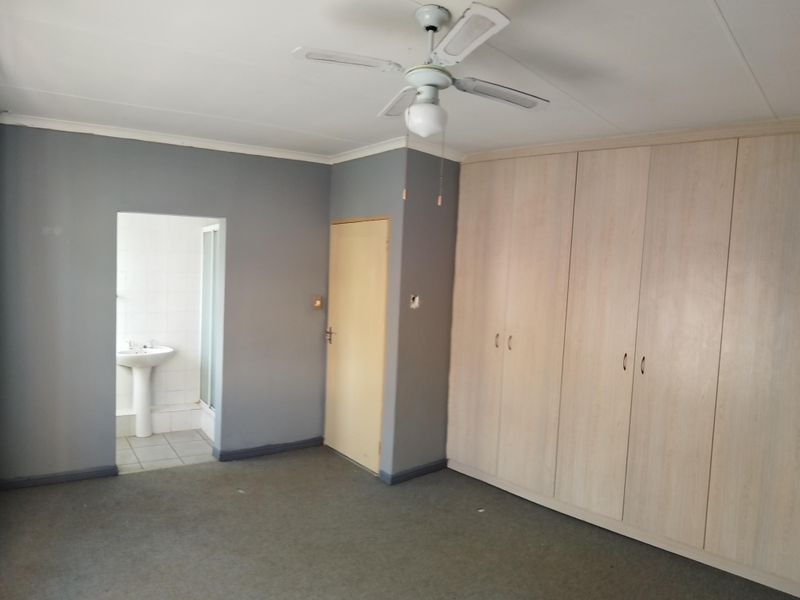 Spacious bedroom featuring built-in cupboards, a ceiling fan, and direct access to an en-suite bathroom with a pedestal basin.