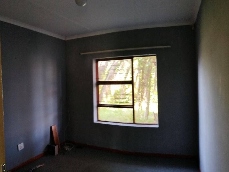 An empty bedroom featuring grey walls, carpeted flooring, and a window with security bars.