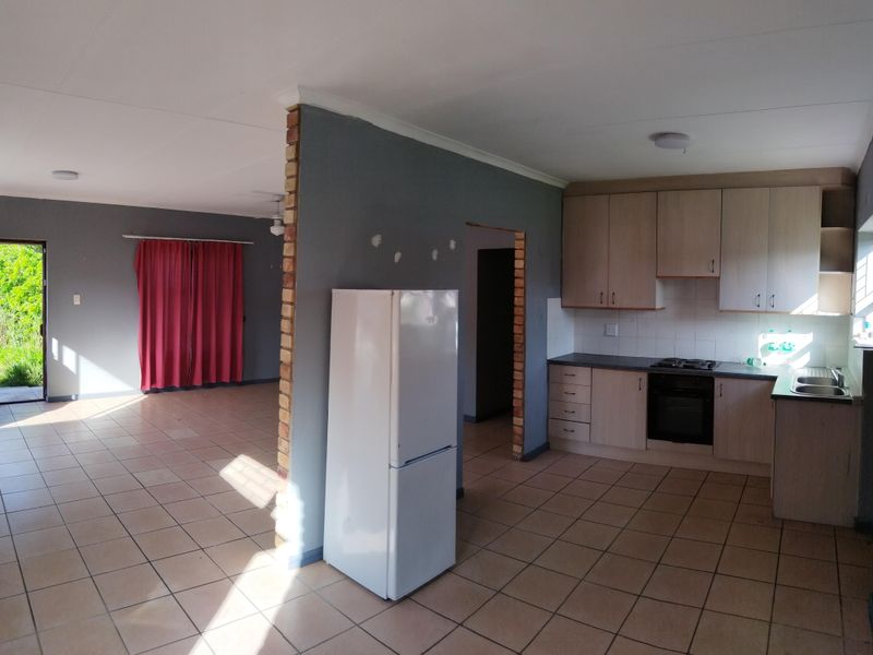 Open plan living and kitchen area featuring tiled flooring, built-in cabinetry, and a central exposed brick pillar, offering a functional layout with potential for updates.