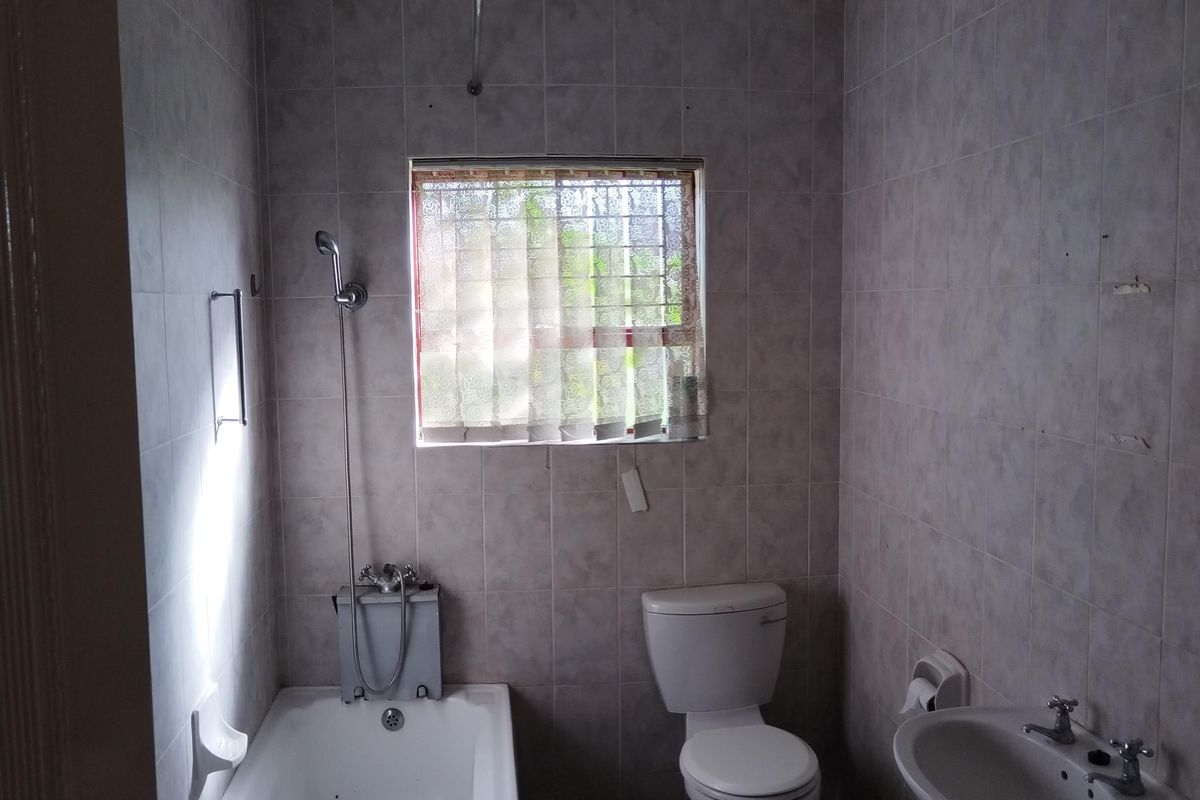 A functional bathroom featuring a bathtub with shower mixer, pedestal basin, and toilet, finished with neutral wall and floor tiling.