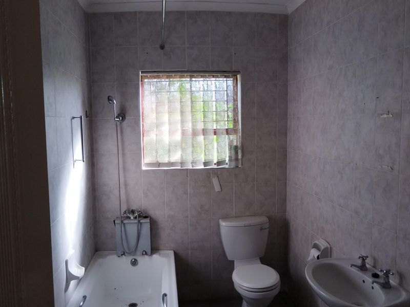 A functional bathroom featuring a bathtub with shower mixer, pedestal basin, and toilet, finished with neutral wall and floor tiling.