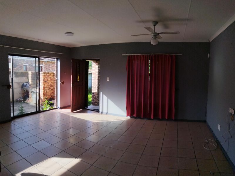 Spacious, empty living area featuring tiled flooring, a ceiling fan, and direct access to the exterior through a sliding glass door and timber entrance door.