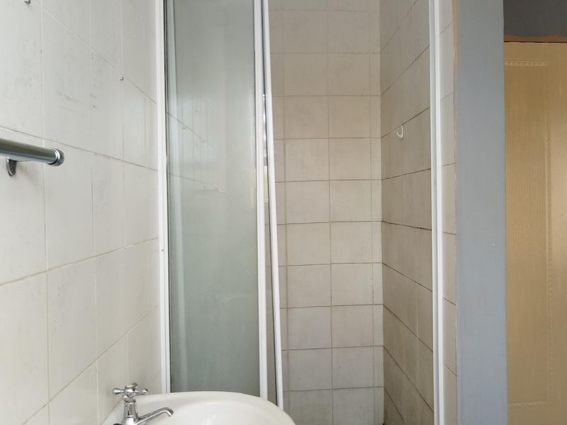A functional bathroom featuring a pedestal basin and a tiled shower enclosure, requiring cosmetic updates to modernize the finishes.