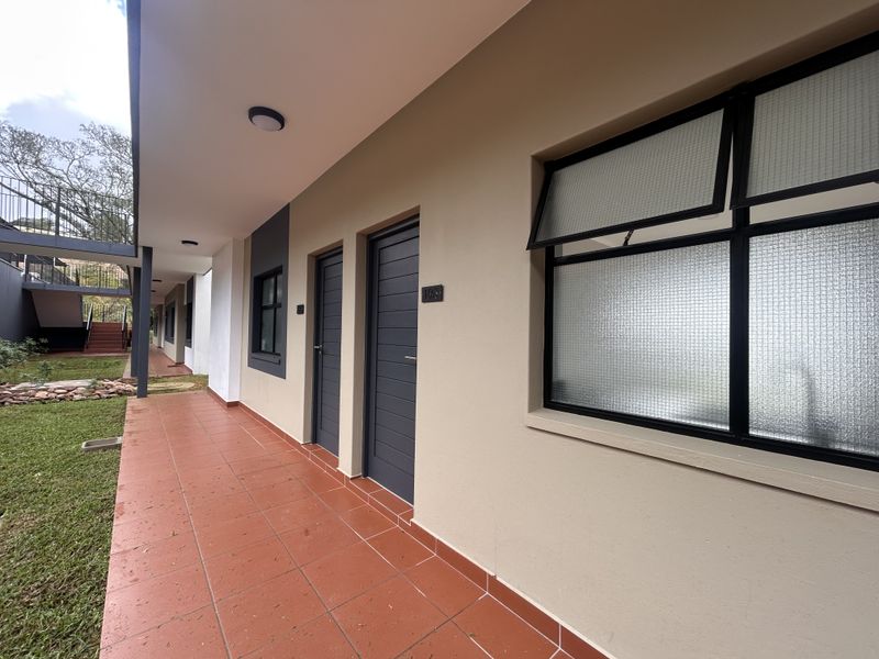 Exterior view of an apartment unit featuring a tiled walkway, modern dark-framed doors, and textured awning windows along the building facade.