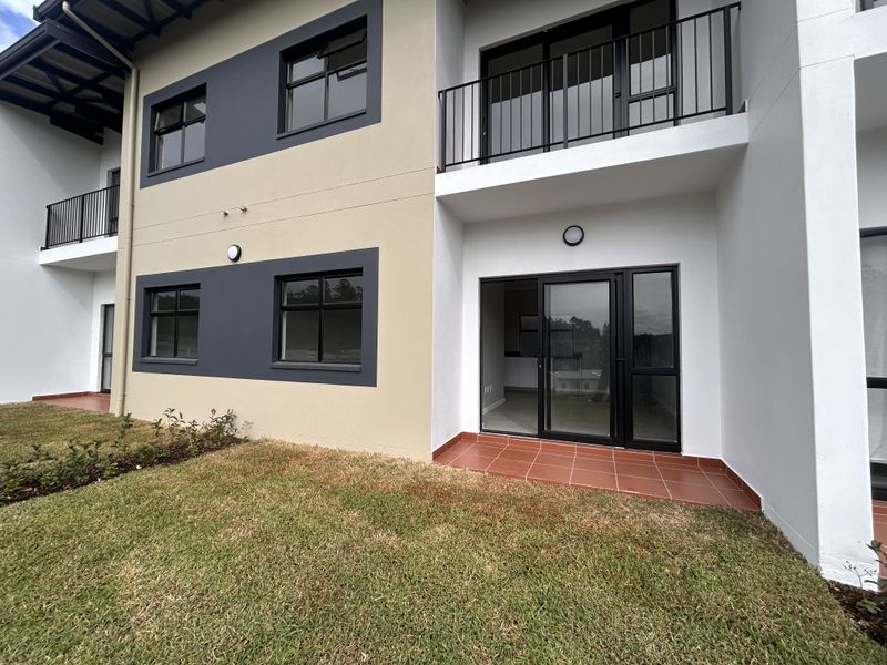 Rear view of a modern apartment building featuring a ground-floor tiled patio, sliding glass doors, and upper-level balconies with metal railings.