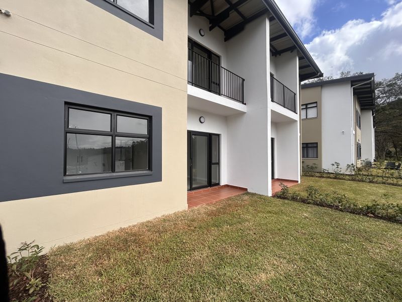 Rear view of a modern apartment building featuring private balconies, tiled patio areas, and well-maintained surrounding lawn.