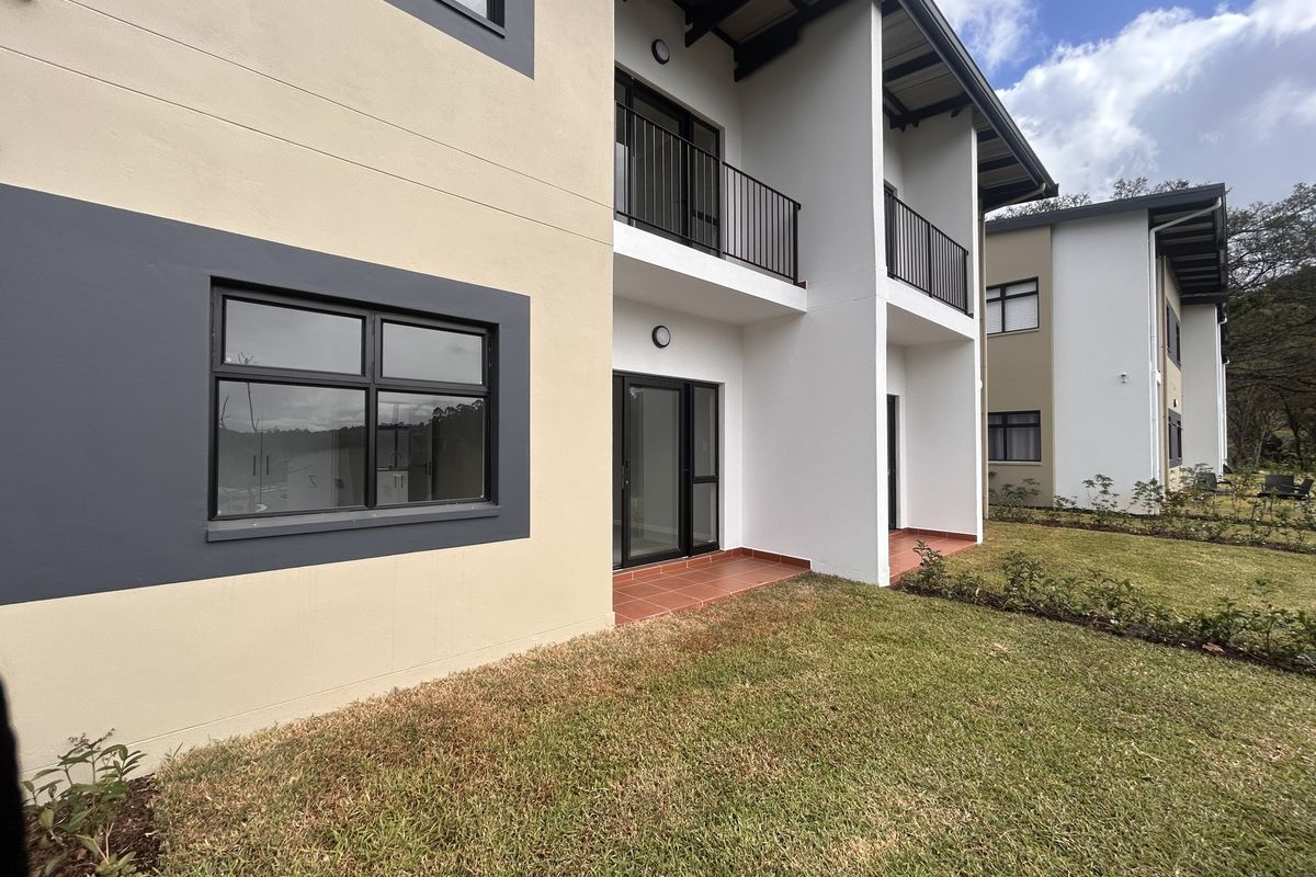 Rear view of a modern apartment building featuring private balconies, tiled patio areas, and well-maintained surrounding lawn.
