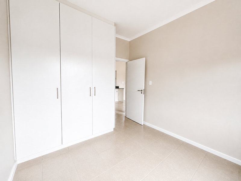 A bright, empty bedroom featuring neutral tiled flooring, built-in white cupboards, and clean wall finishes, offering a versatile space ready for personalization.