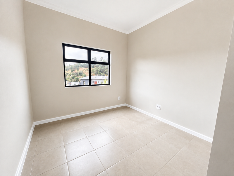 A bright, empty bedroom featuring neutral-toned tiled flooring, clean walls, and a black-framed window offering a view of the surrounding area.