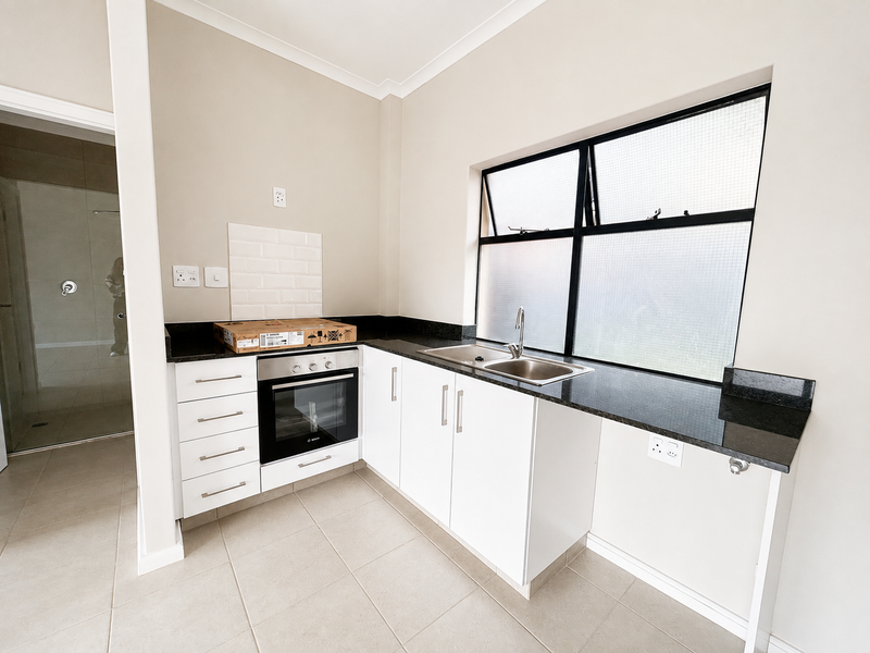 A clean, modern kitchen featuring white cabinetry, granite countertops, a built-in oven, and a tiled backsplash, offering a functional and bright workspace.
