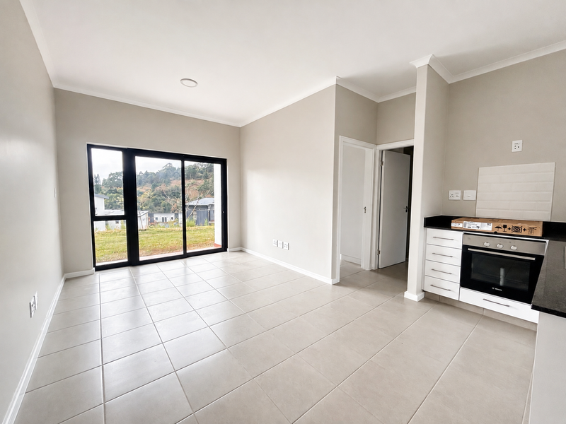 Bright open-plan living and kitchen area featuring neutral tiled floors, modern cabinetry, built-in oven, and large sliding doors leading to an outdoor view.