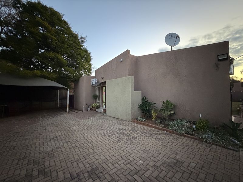 Front exterior view featuring a paved driveway, carport, and stucco facade with integrated security lighting and satellite dish.