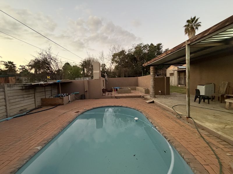 Outdoor pool area featuring a swimming pool, brick paving, a covered patio, and a built-in braai, offering potential for renovation and landscaping.