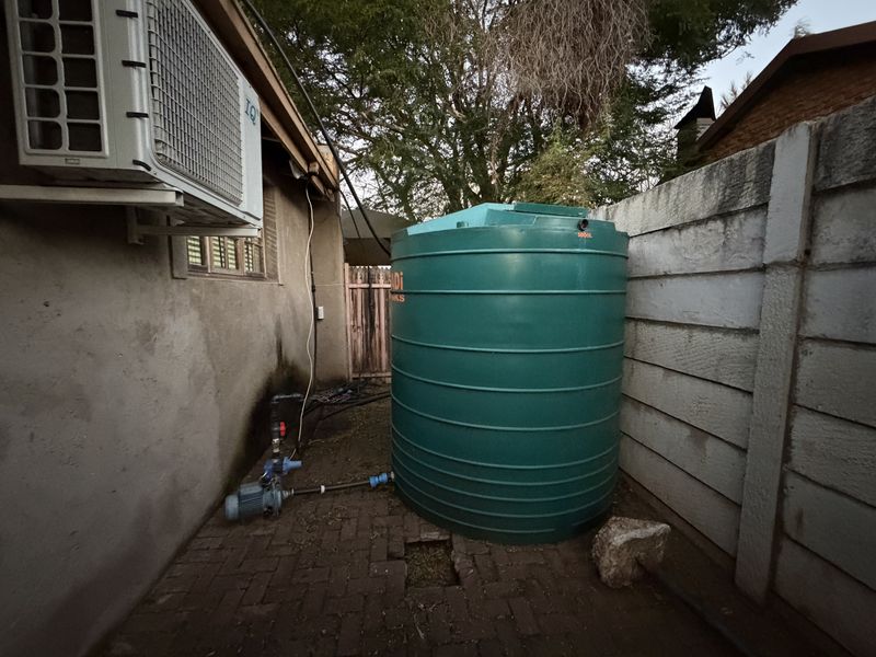 Rear exterior area featuring a large water storage tank with pump system, air conditioning unit, and precast concrete boundary walling.