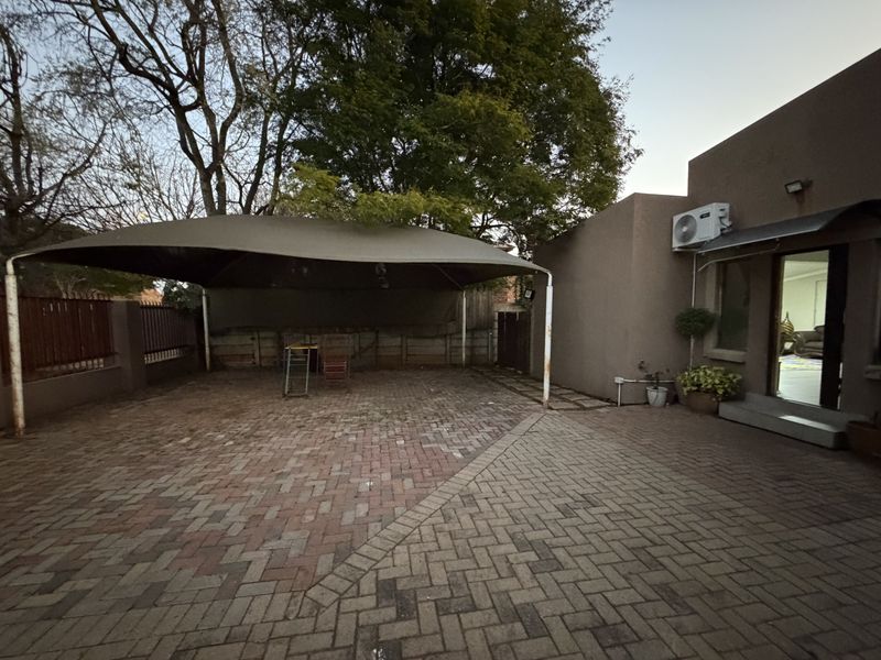 Rear exterior area featuring a paved driveway, a large shade sail structure, and an external air conditioning unit mounted on the wall.