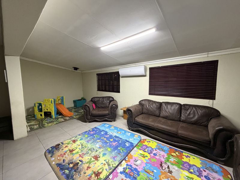 A spacious living area featuring tiled flooring, a wall-mounted air conditioning unit, and venetian blinds, providing a functional space for family activities.
