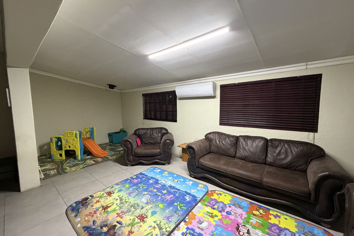A spacious living area featuring tiled flooring, a wall-mounted air conditioning unit, and venetian blinds, providing a functional space for family activities.