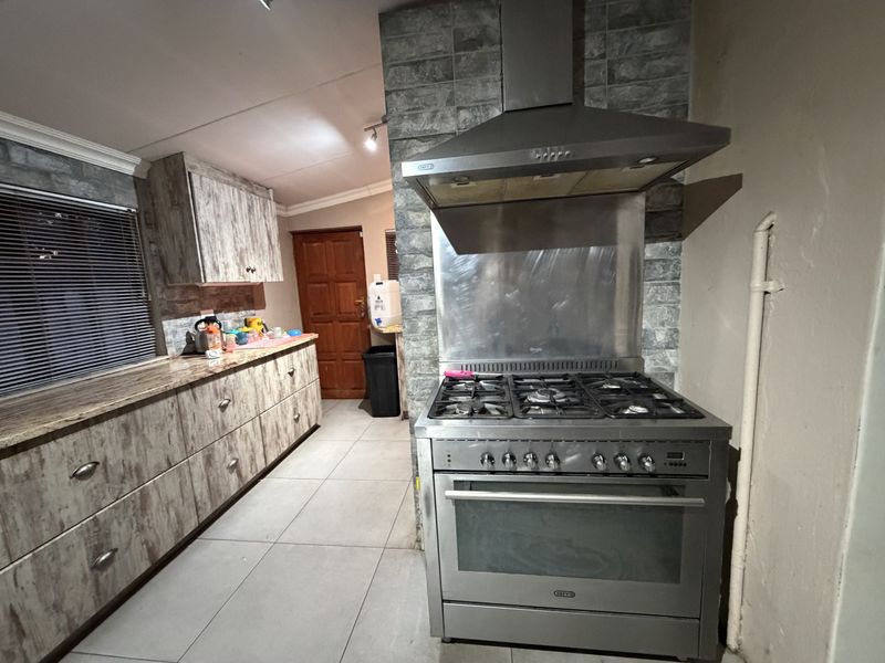 A functional kitchen featuring a stainless steel gas stove, extractor fan, stone-look cabinetry, and tiled flooring with an exposed wall pipe.