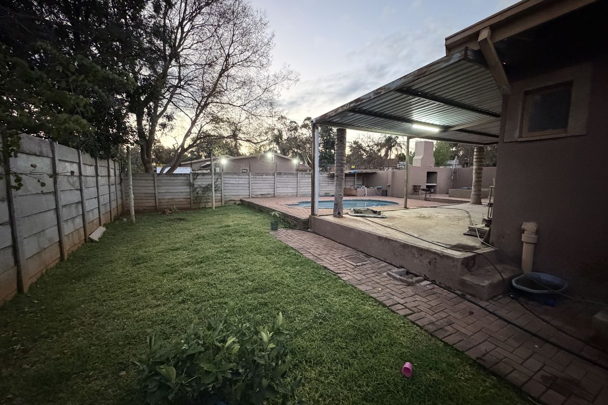 Rear garden featuring a swimming pool, covered patio area with built-in braai, and paved pathways enclosed by precast concrete walling.