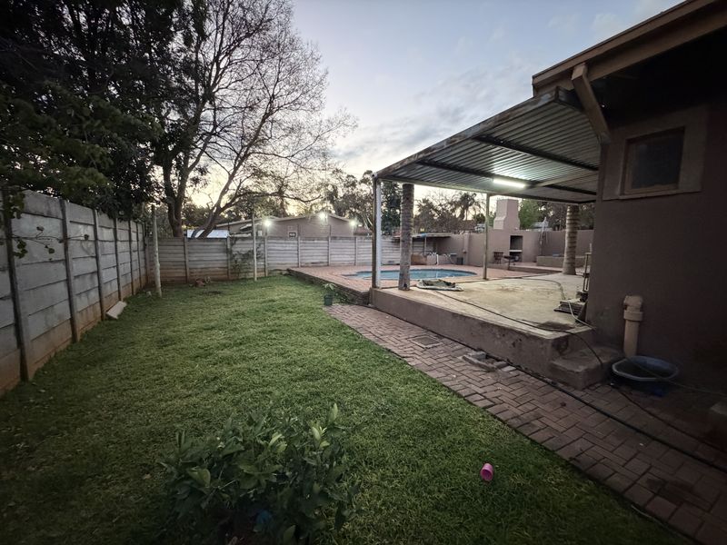 Rear garden featuring a swimming pool, covered patio area with built-in braai, and paved pathways enclosed by precast concrete walling.