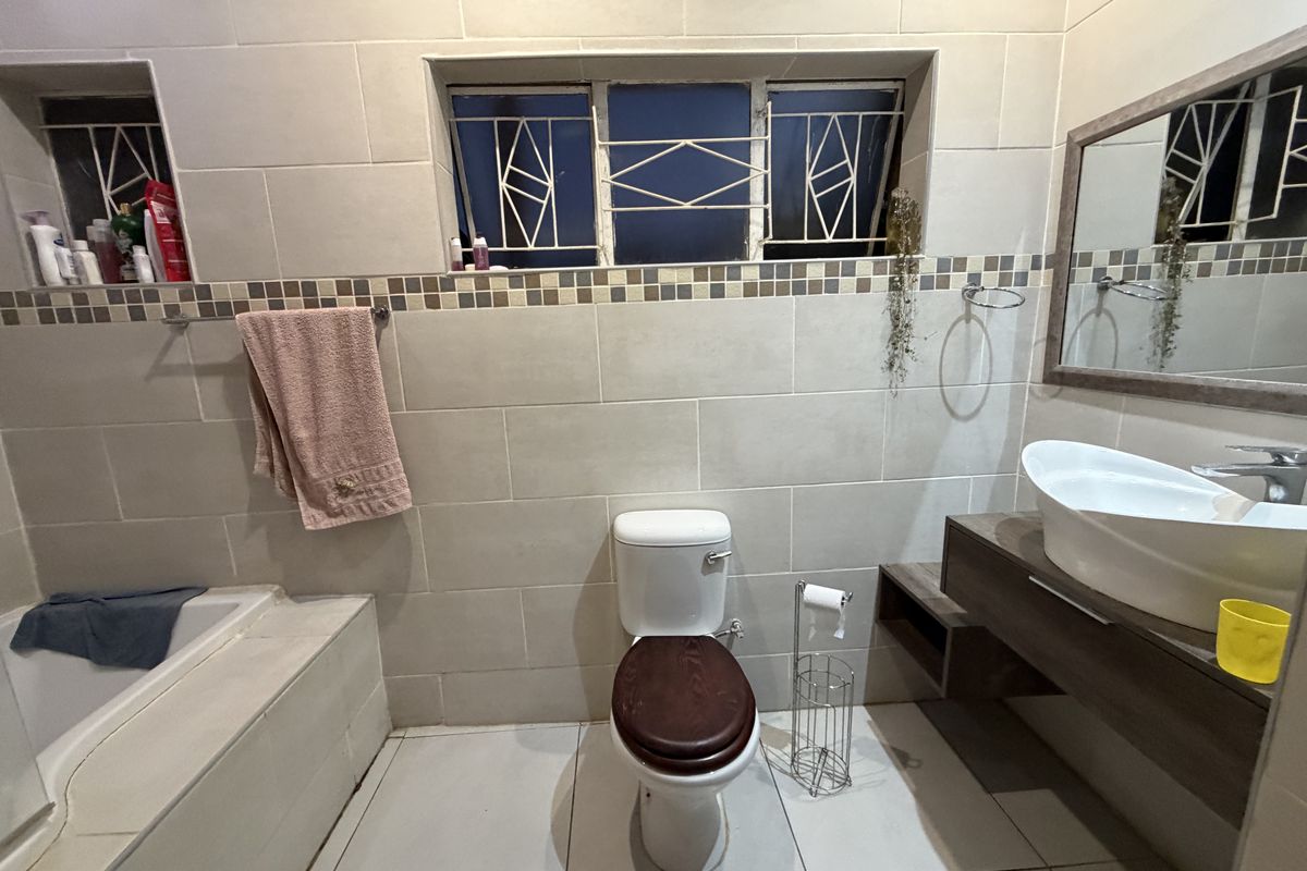 A functional bathroom featuring a built-in bathtub, wall-mounted vanity with a vessel sink, and neutral ceramic tiling throughout.