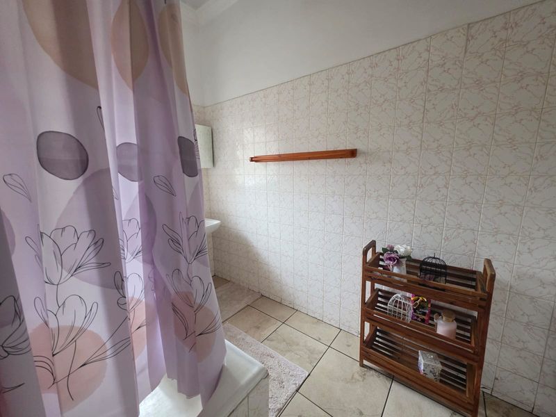 A functional bathroom featuring tiled walls and flooring, a bathtub with a shower curtain, and a pedestal basin.